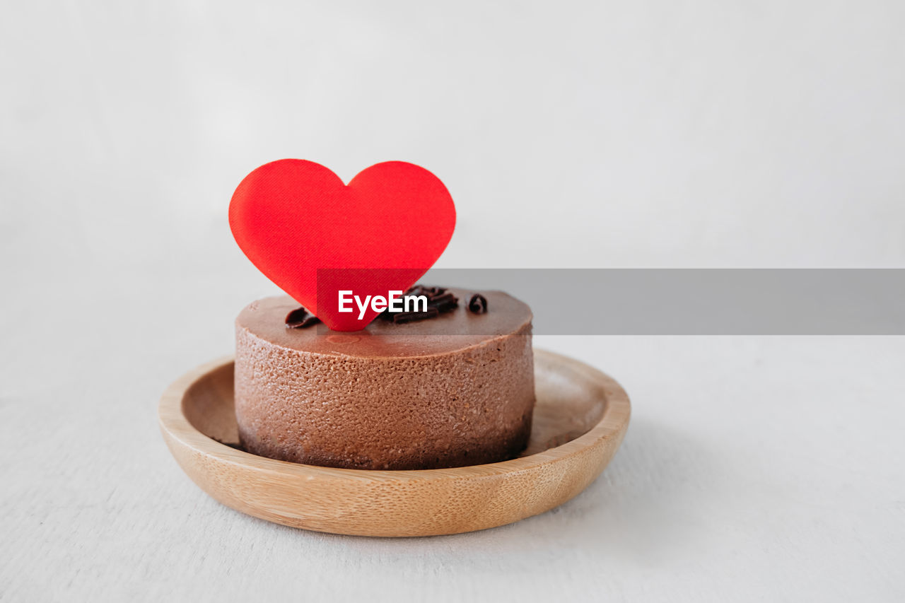 Red heart decoration on round small chocolate cheesecake without baking on bamboo plate