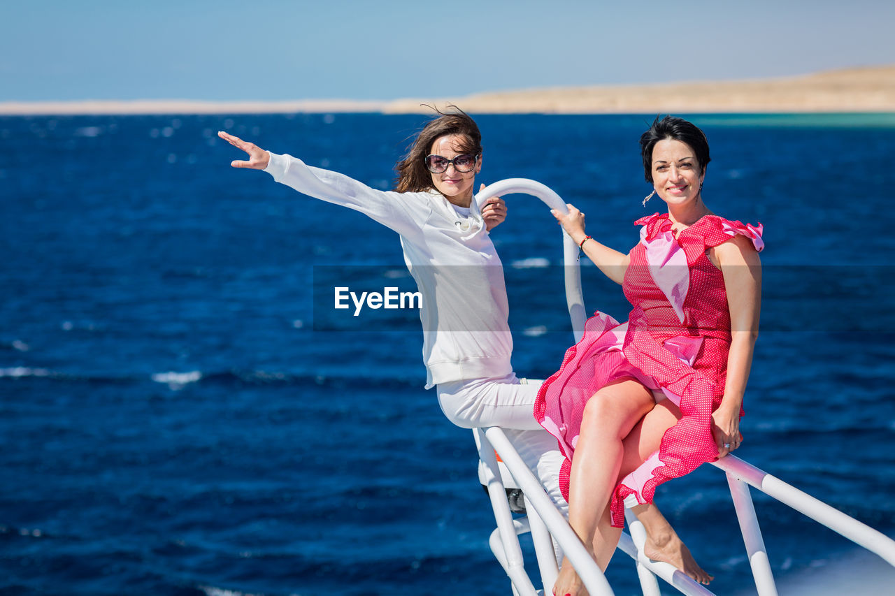 Two women relaxing together on the nose of the yacht at sunny summer day at sea