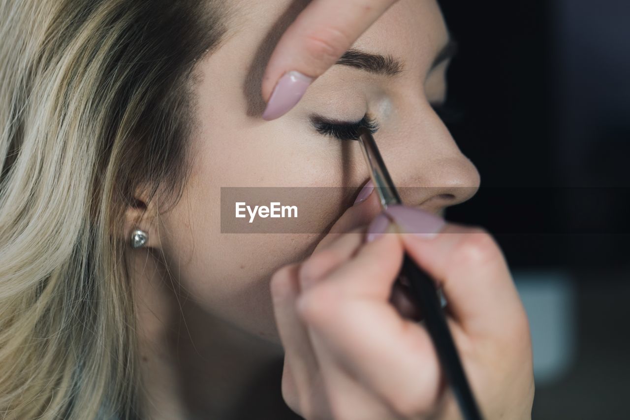 Cropped hands applying eyeliner to woman