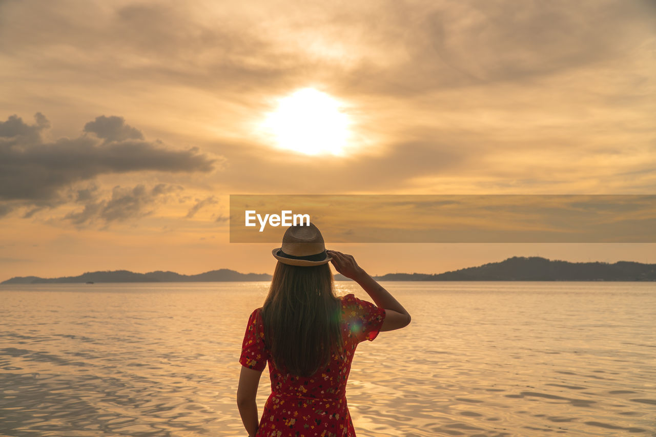 Rear view of woman standing against sea during sunset