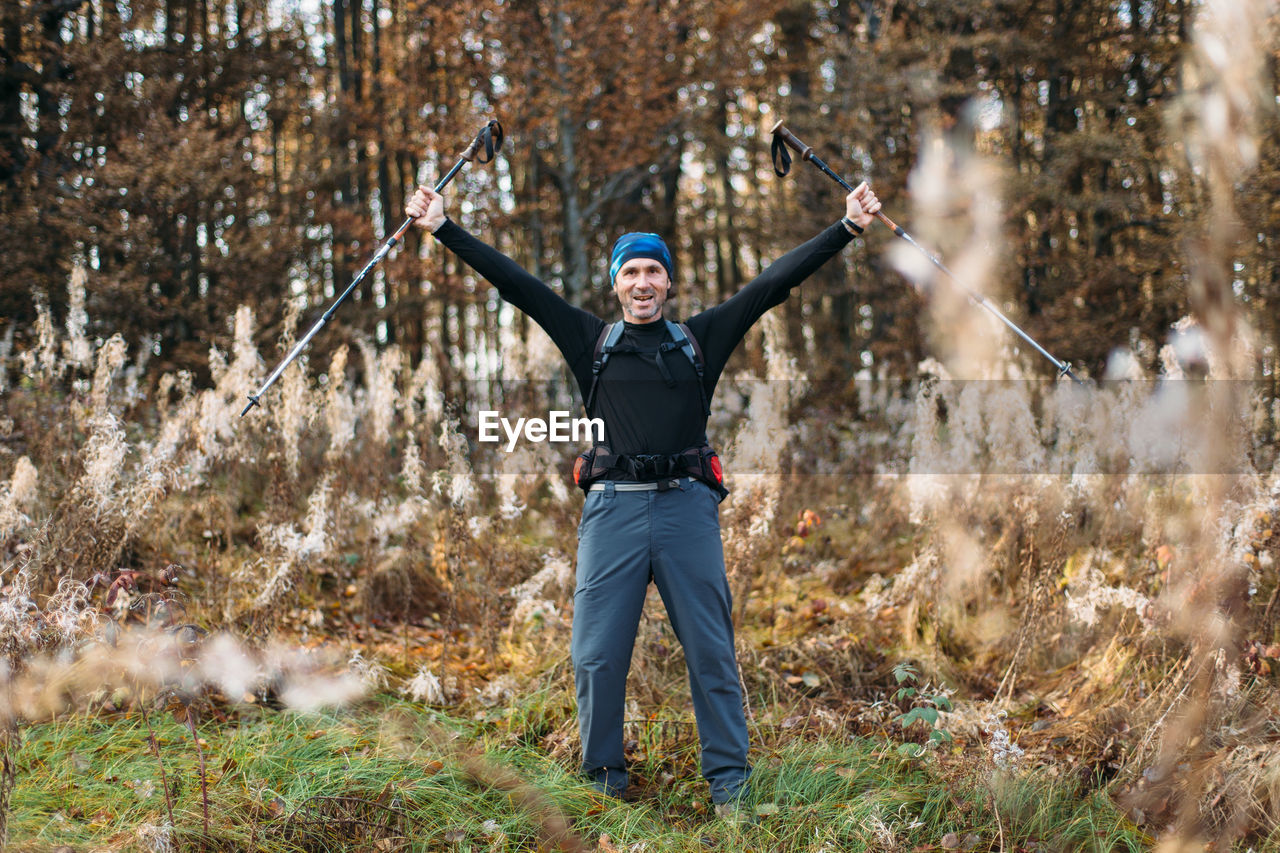 Portrait of happy mature man with trekking poles in autumn forest