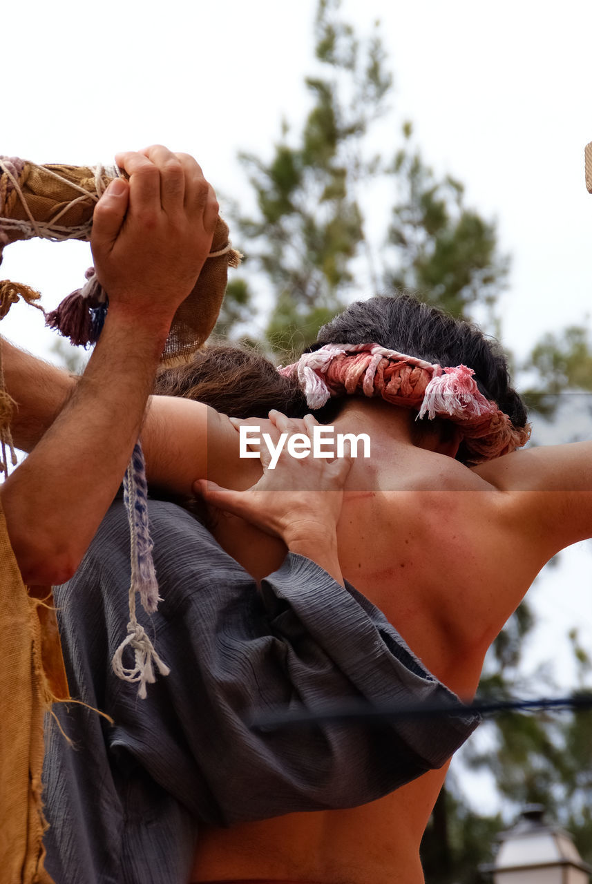 Rear view of people carrying man for crucifix outdoors