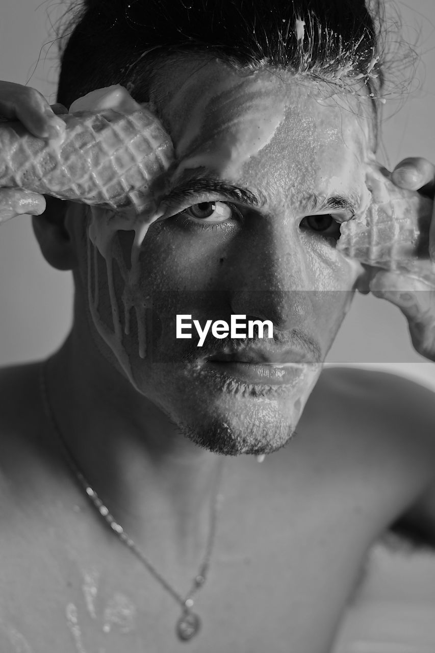 Close-up portrait of shirtless man face covering by ice cream indoors