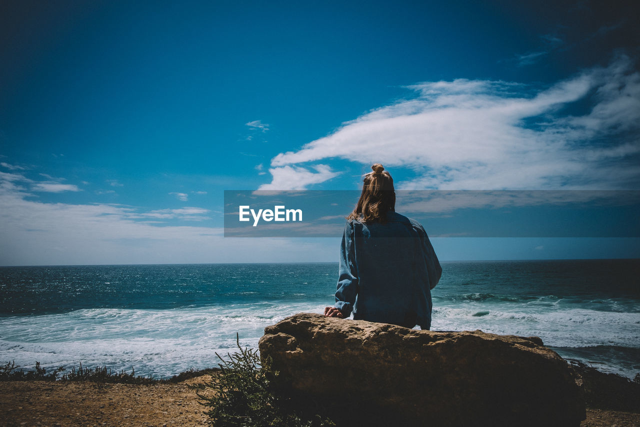Rear view of woman sitting on rock against sea at beach