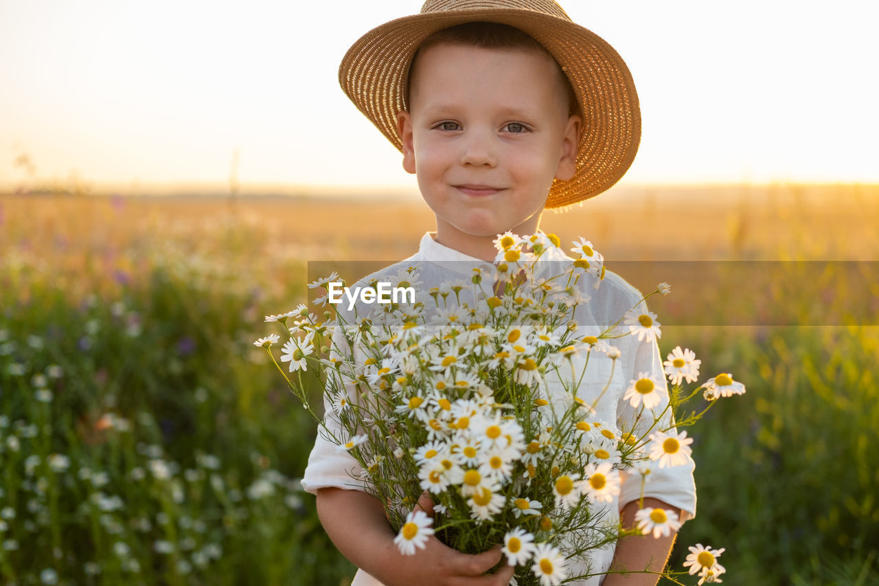 Portrait of cute boy holding flowers at field