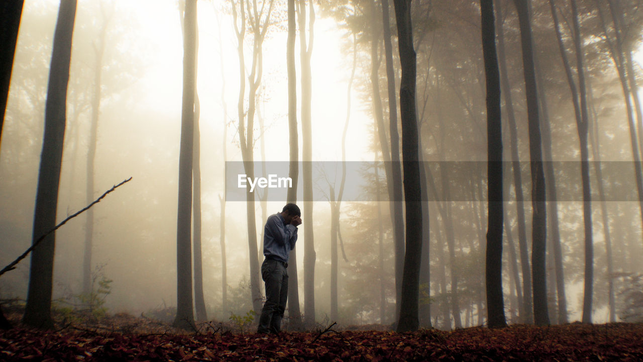 Depressed man standing in forest during foggy weather