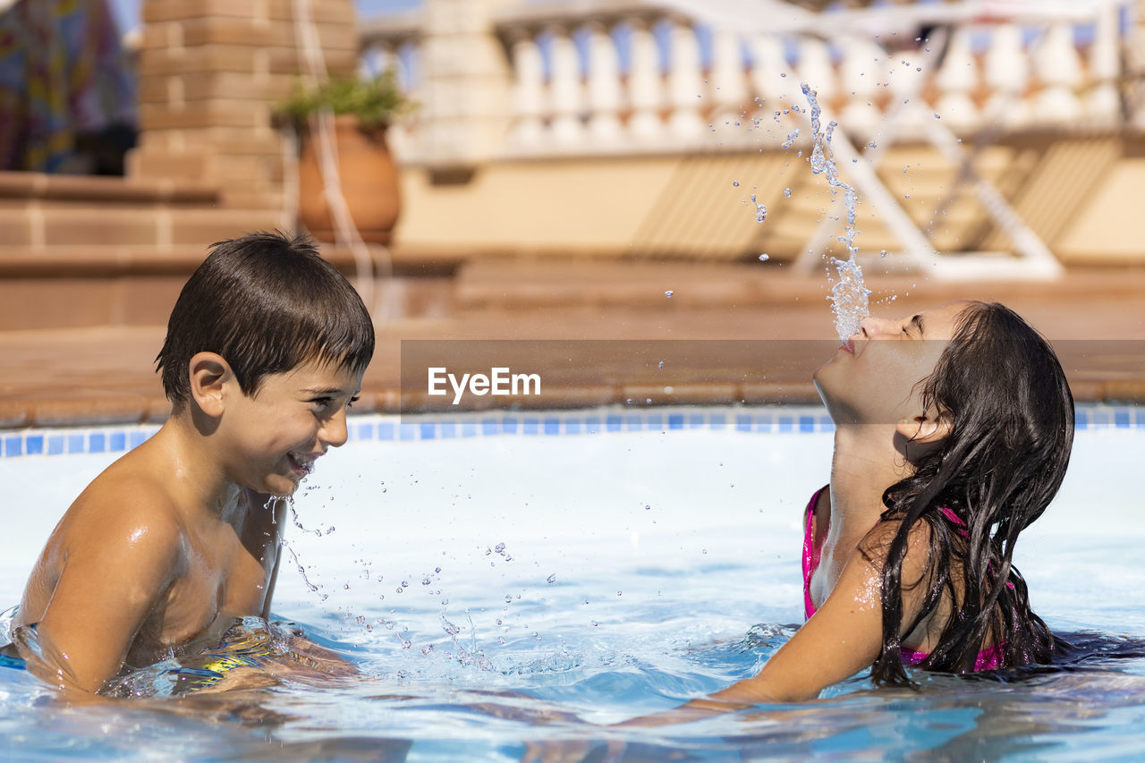 Two friends spitting water from mouth in a pool