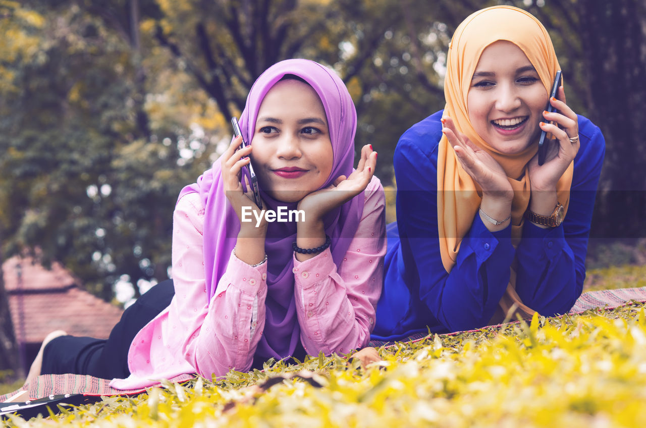  friendship and happiness concept. portrait of smile young muslimah laying on grass at city park