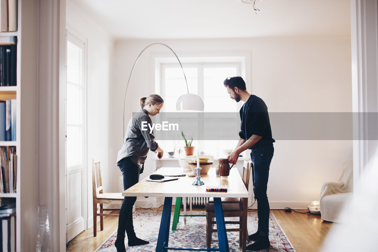 Side view of couple arranging objects on dining table at home