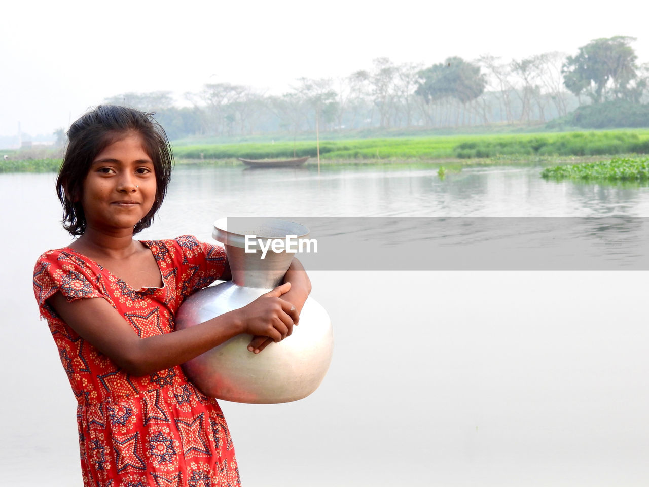 Portrait of young woman drinking water while standing against lake