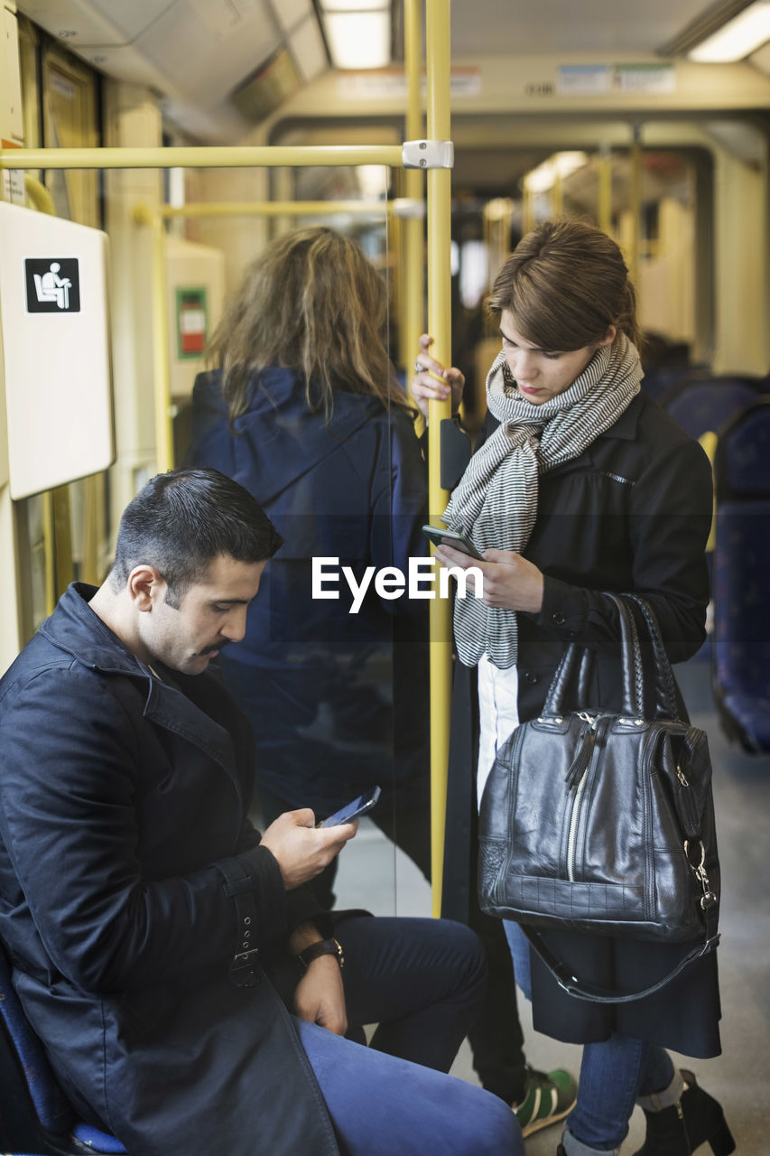 Male and female passengers using mobile phone in tram