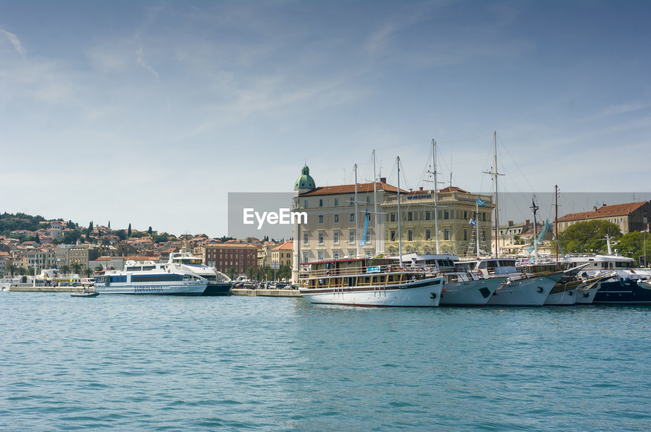 SAILBOATS IN HARBOR BY BUILDINGS AGAINST SKY