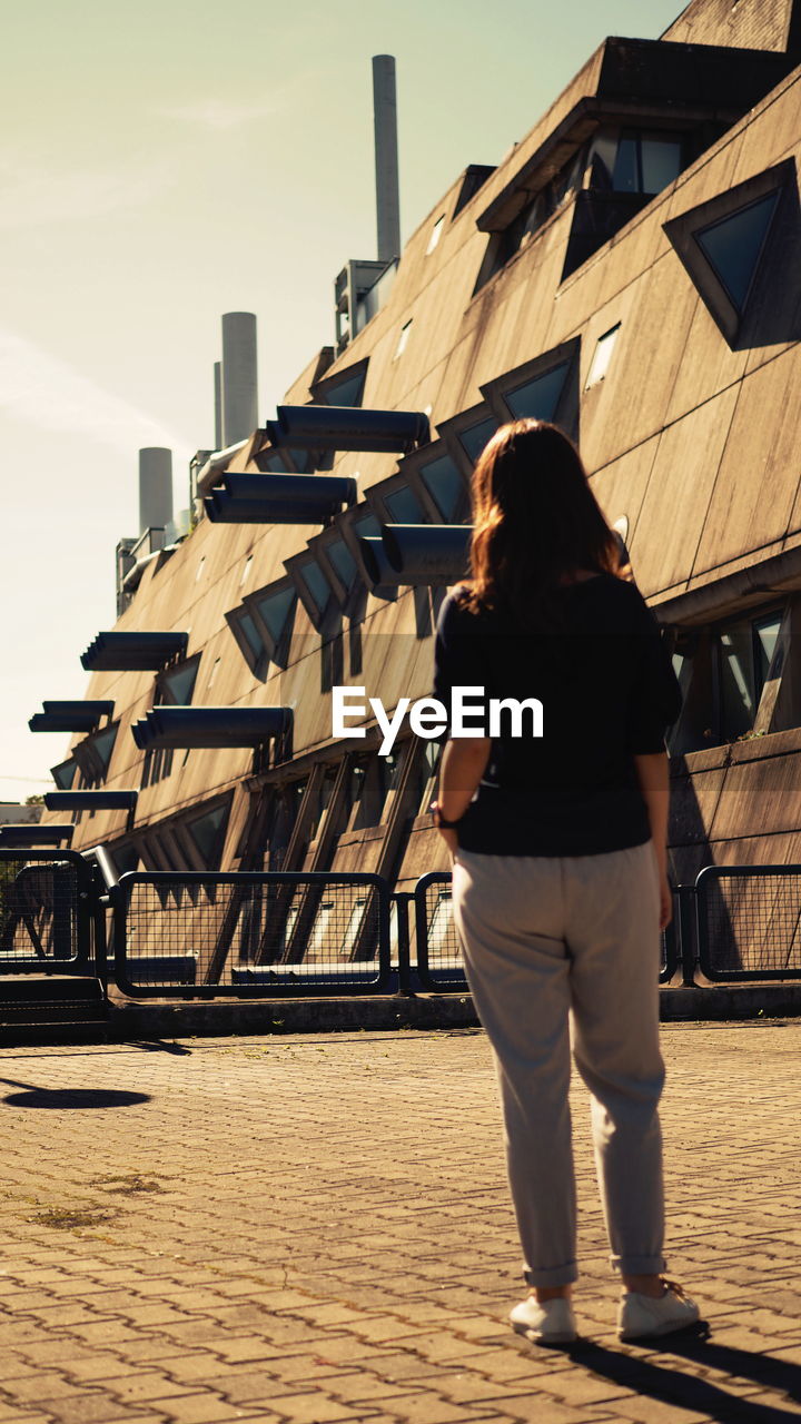 REAR VIEW OF WOMAN STANDING AGAINST BUILDING