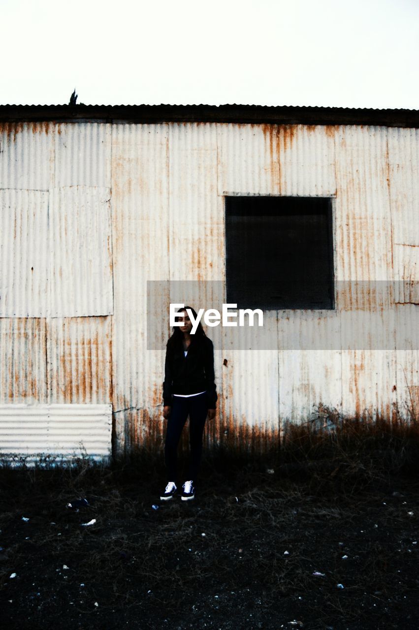 FULL LENGTH OF YOUNG WOMAN STANDING BY WALL