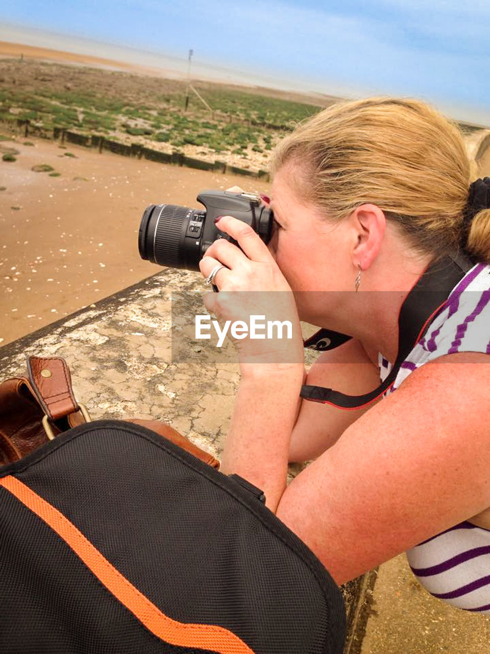 Woman photographing with camera while leaning retaining wall