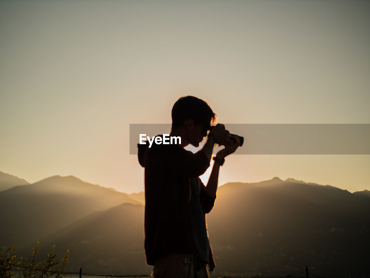 Man photographing on mountain against sky during sunset