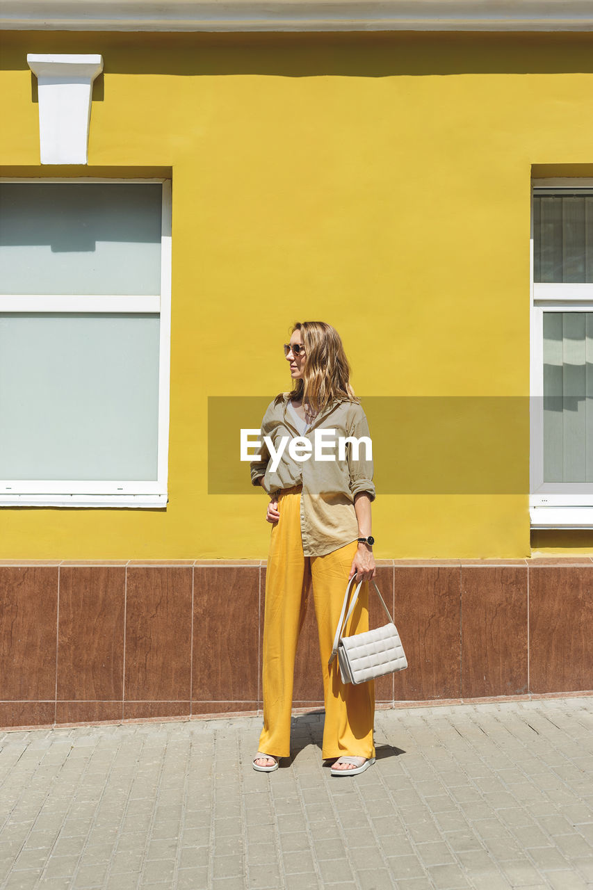 Full length of woman standing against yellow wall