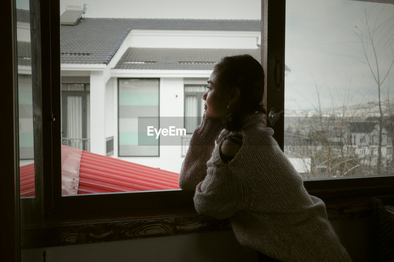 young woman looking through window at home