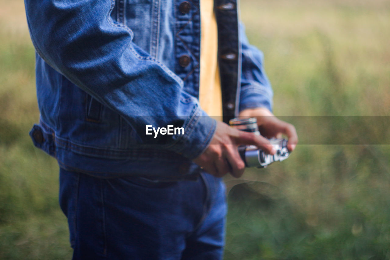 Male hands holding retro photo camera on green nature background. film grain effect. man in jeans 