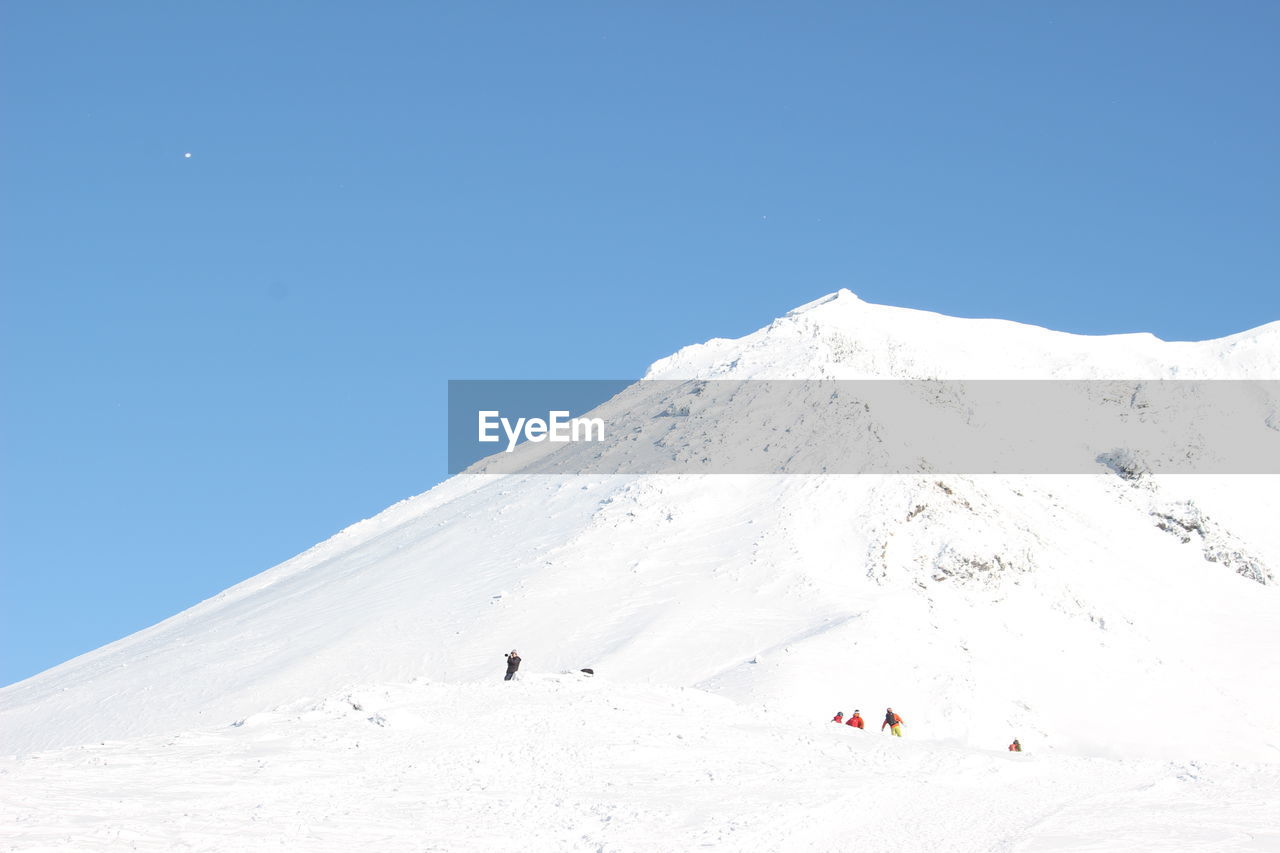 People on snowcapped mountain against clear blue sky