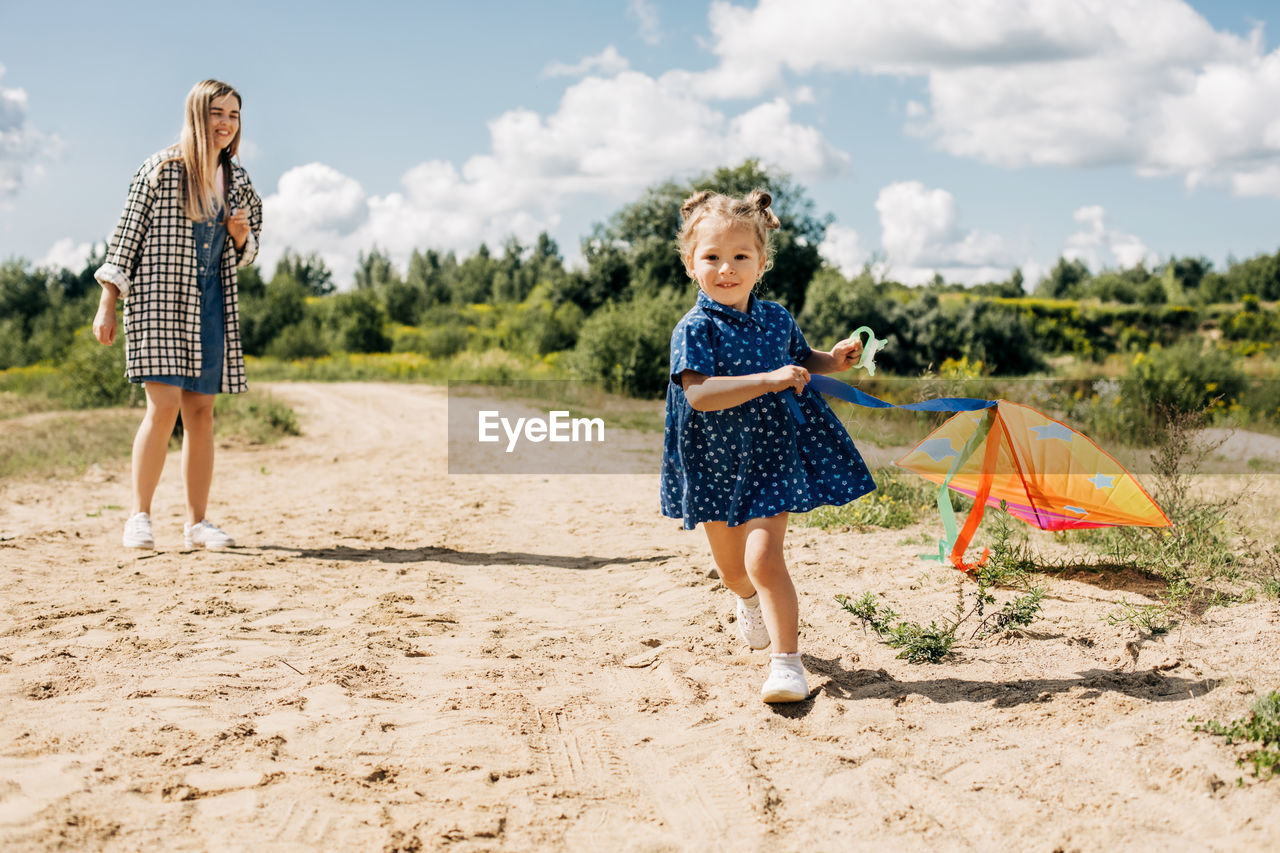 A little girl flies a kite with her older sister and runs away from her