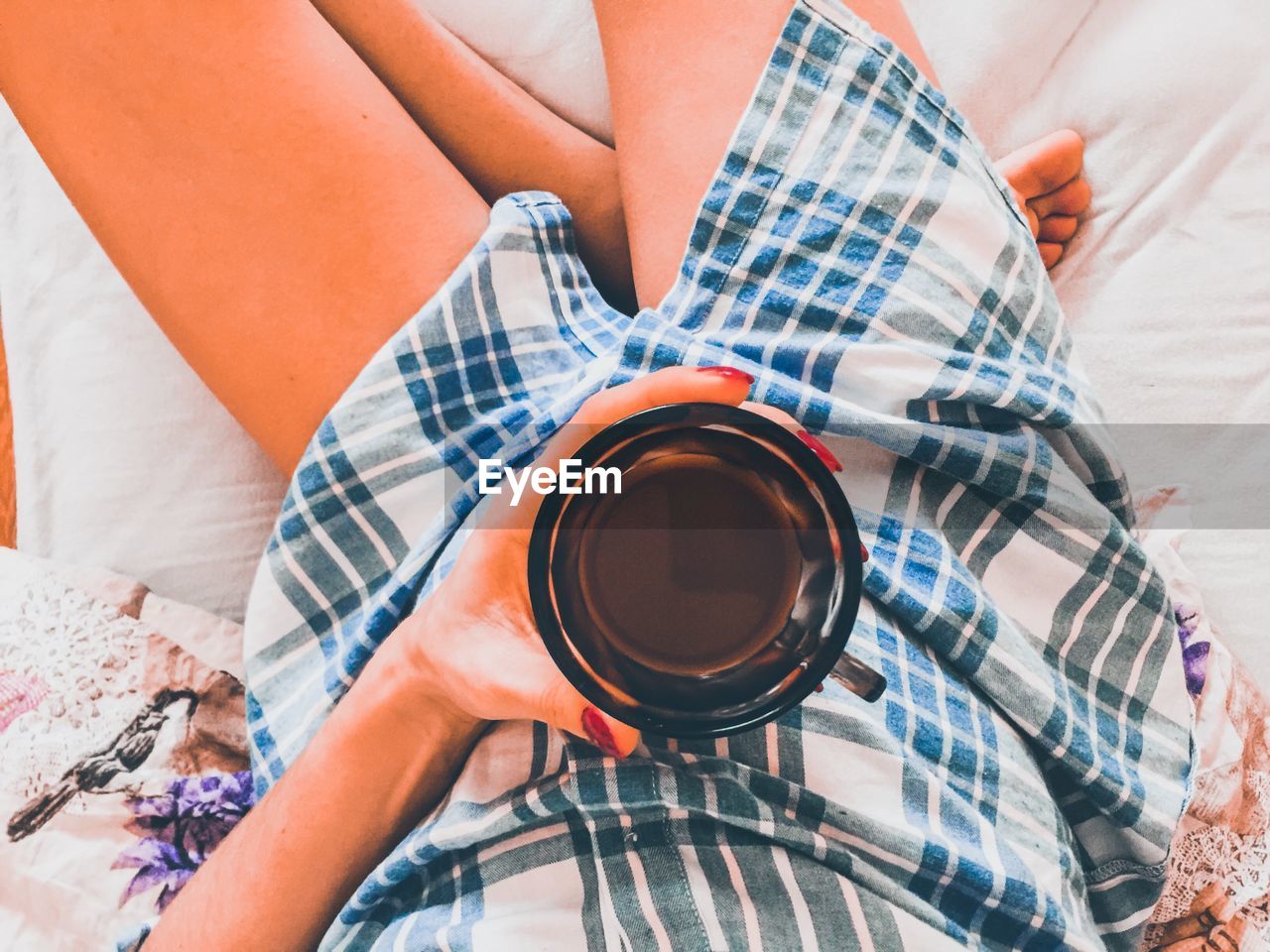 Low section of woman drinking coffee on bed
