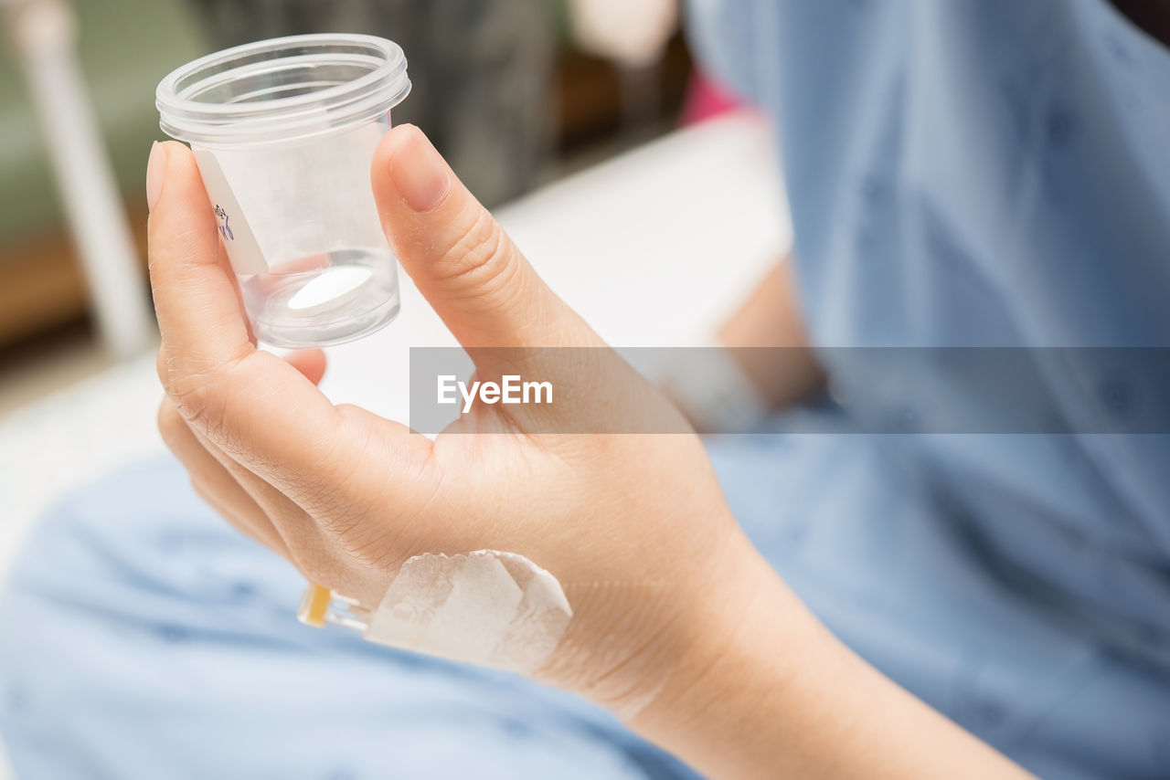 Close-up of hand holding cup with pill