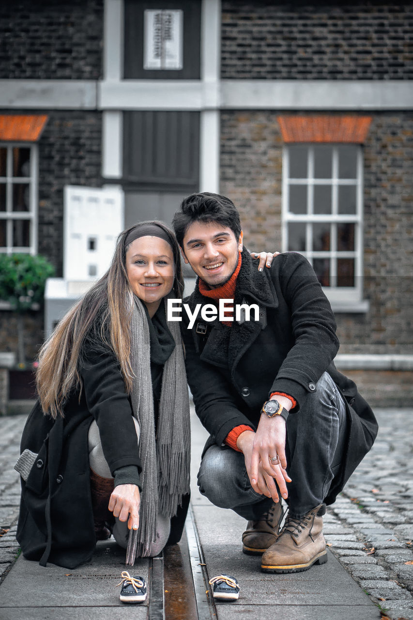 Portrait of smiling man and woman crouching on walkway