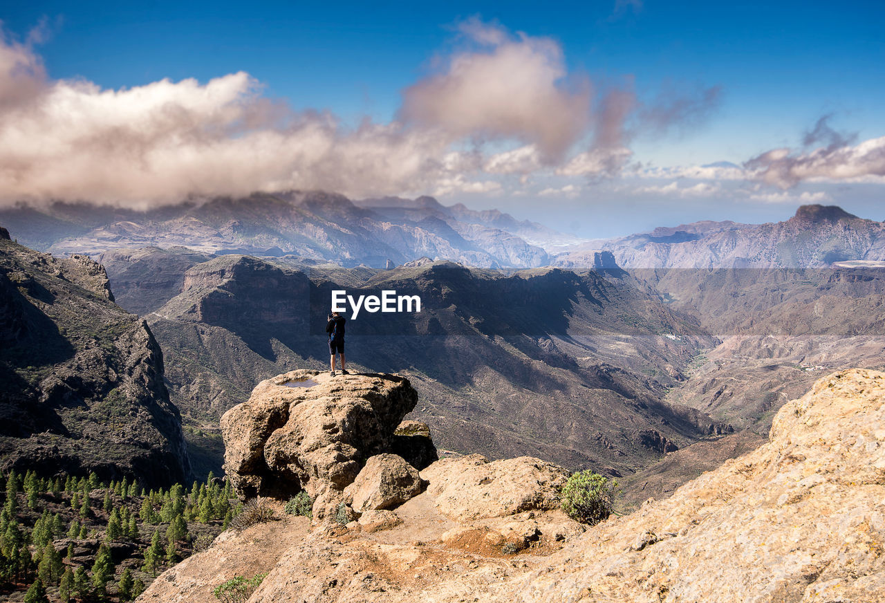 Mid distance view of person standing on cliff against mountains