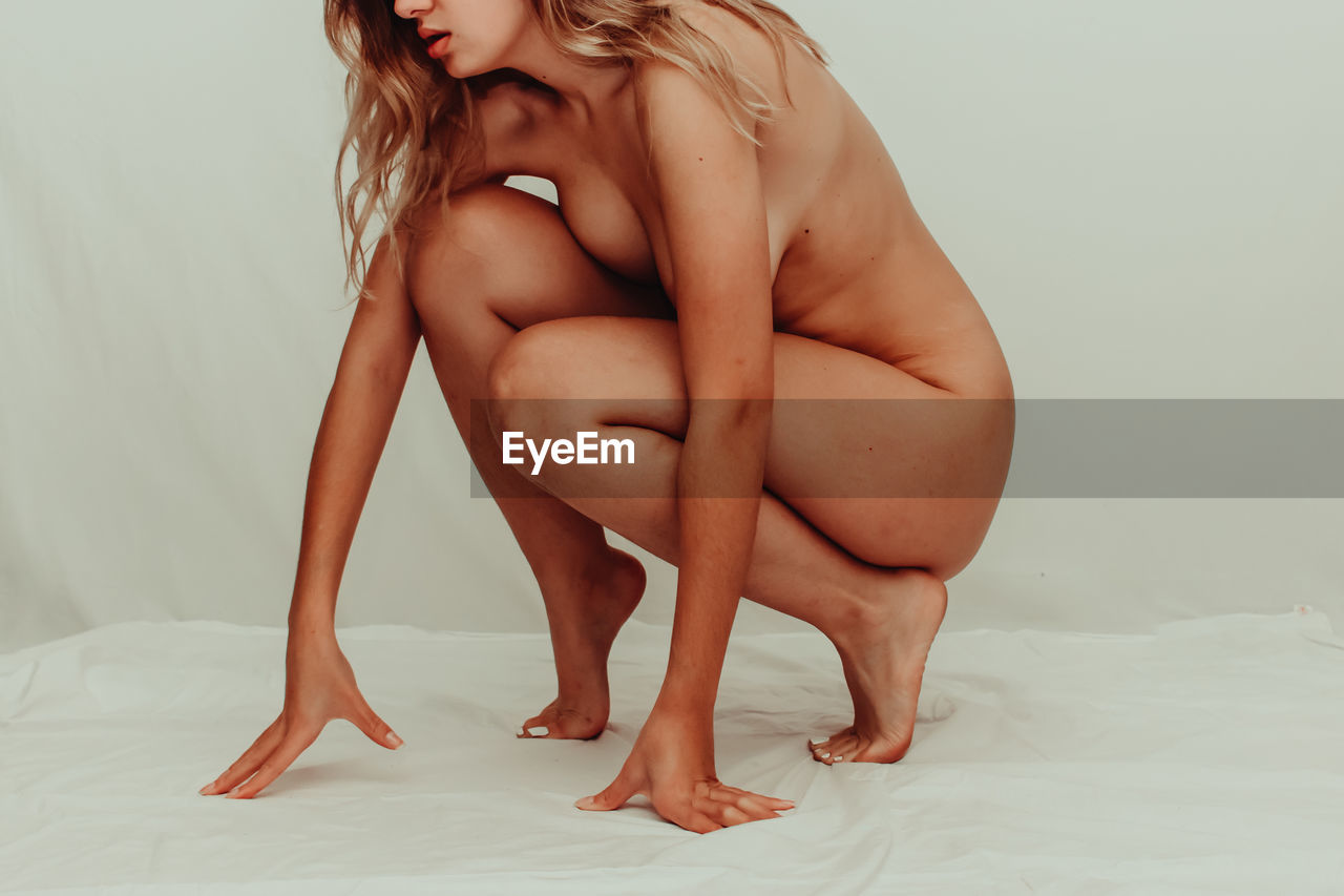 Low section of naked woman on bed at home