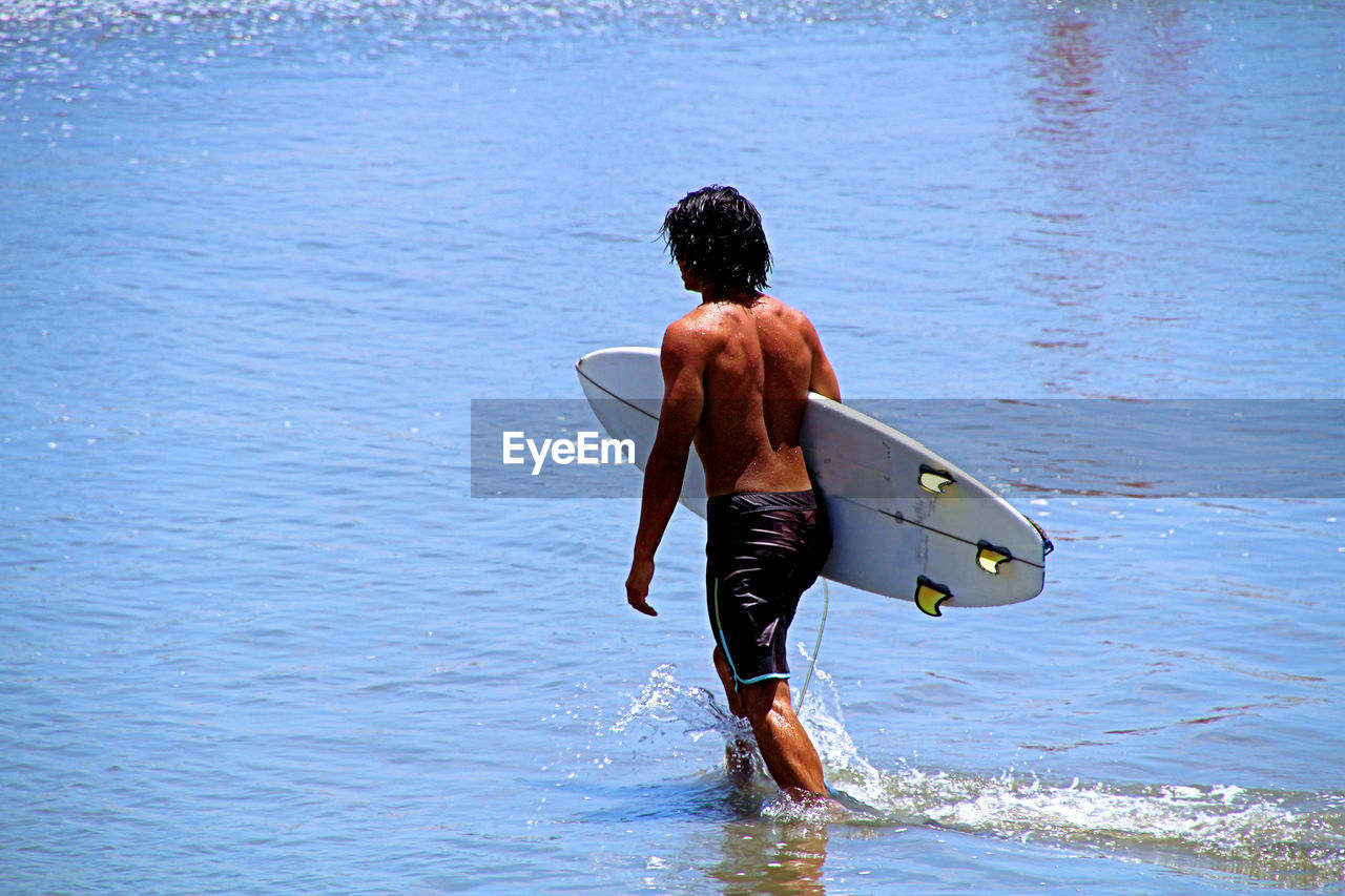 REAR VIEW OF SHIRTLESS MAN IN WATER