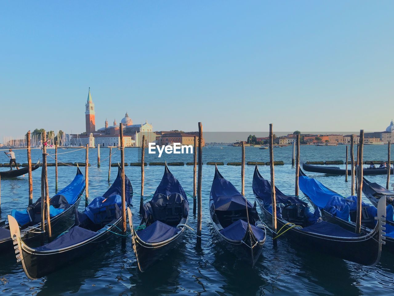 Gondolas moored at canal against clear sky