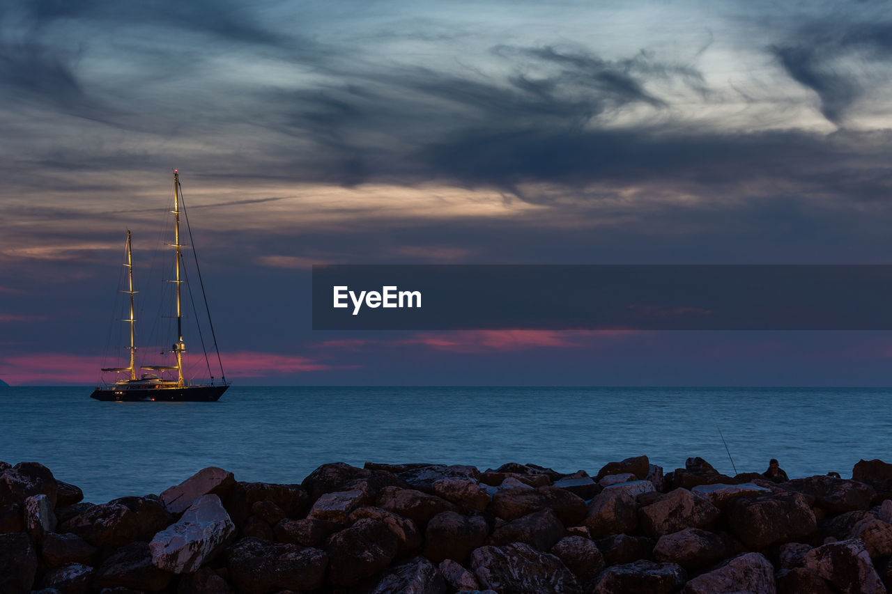 Sailboat on sea against cloudy sky during sunset