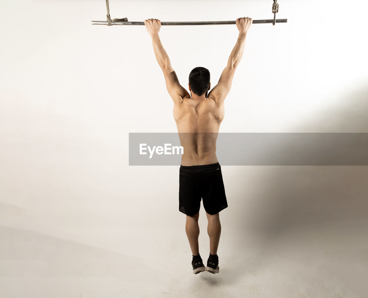 REAR VIEW OF SHIRTLESS MAN WITH ARMS RAISED STANDING