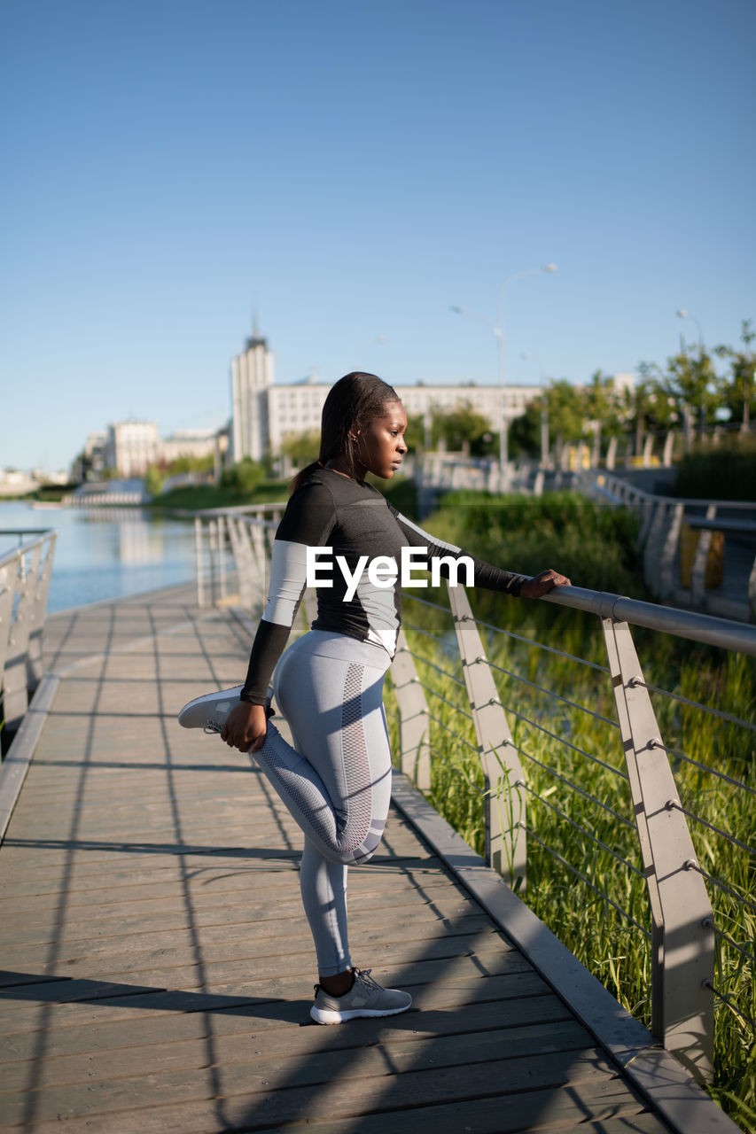 Ethnic sportswoman stretching on embankment