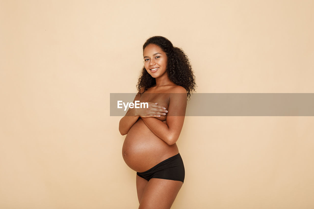 Portrait of shirtless pregnant woman against beige background