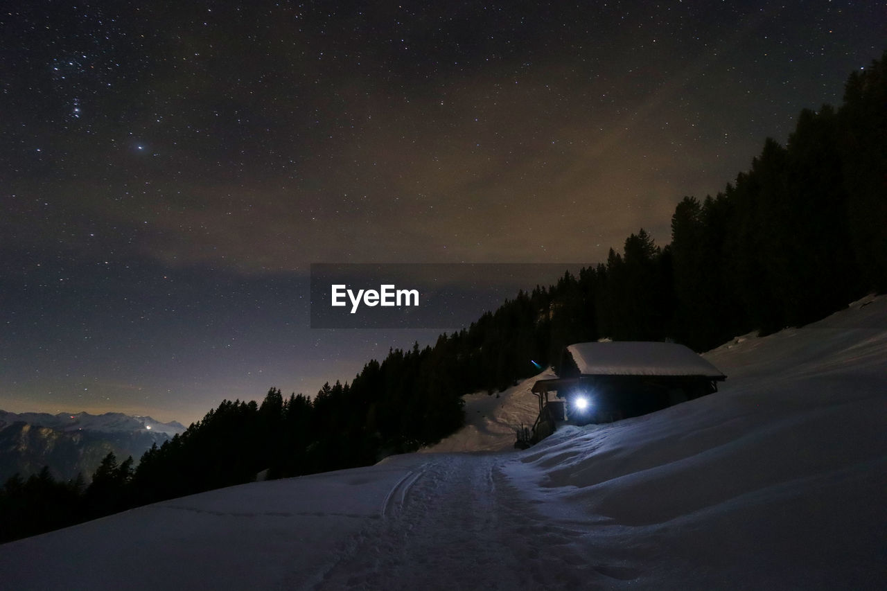 Snow covered cabin against sky at night