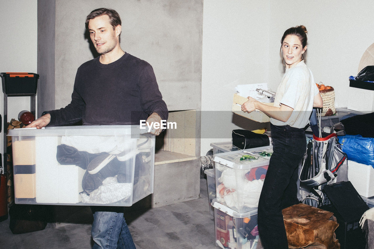 Man and woman helping each other while picking boxes during relocation of house