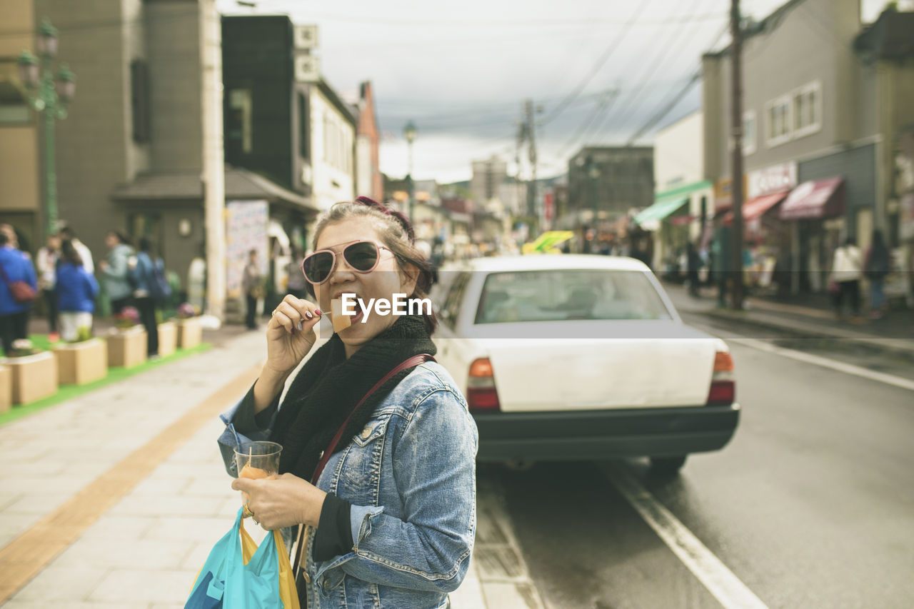 Portrait of woman eating food on street in city