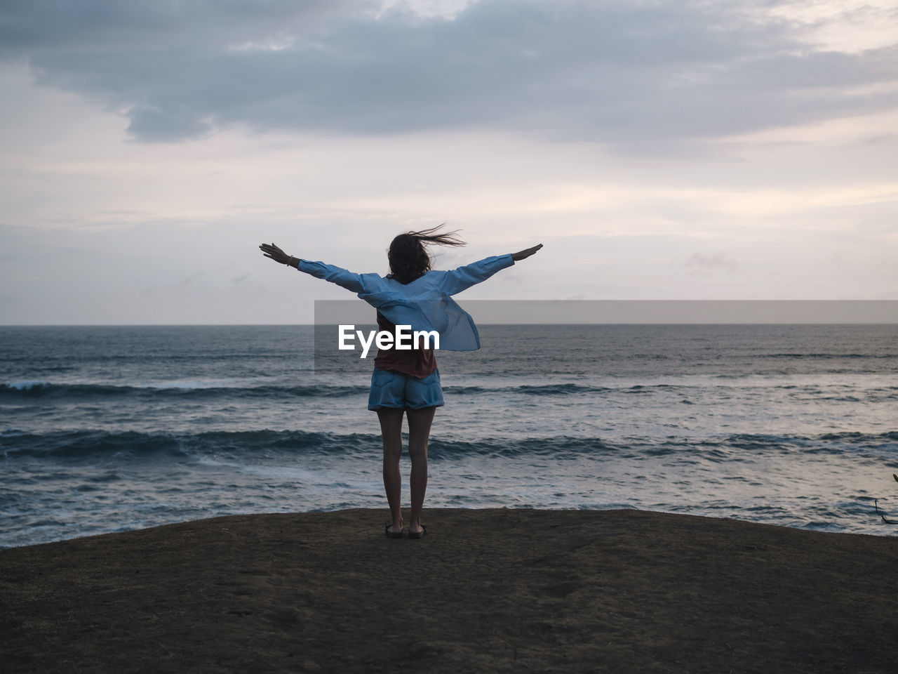 Woman with raised arms standing at the sea at sunset