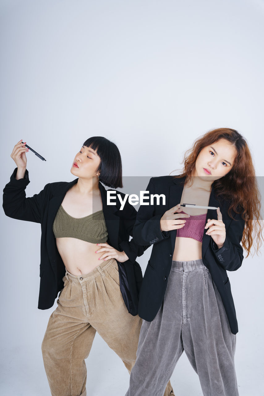 Portrait of lesbian couple holding pen standing against gray background