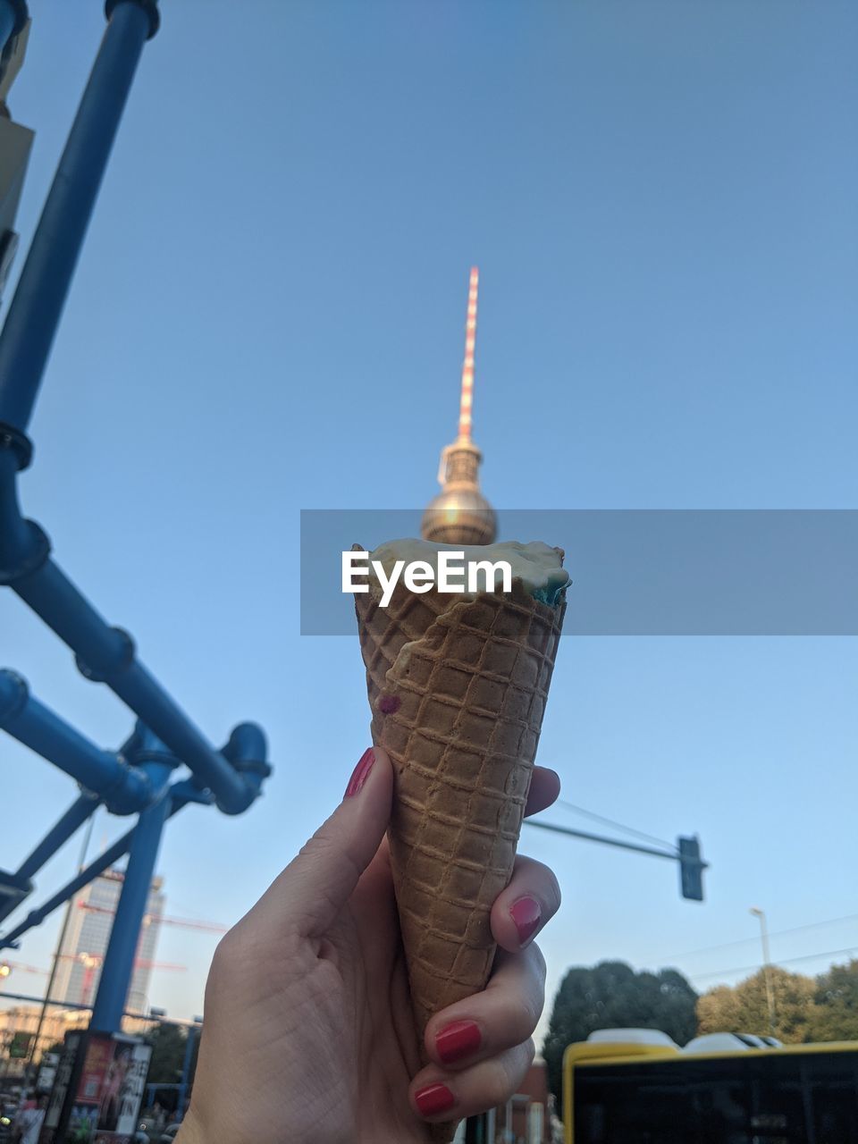 ice cream cone, hand, cone, frozen food, ice cream, architecture, holding, sky, frozen, sweet food, one person, city, built structure, personal perspective, nature, day, sweet, dairy, clear sky, food and drink, tower, building exterior, outdoors, food, travel destinations, leisure activity, adult, fast food