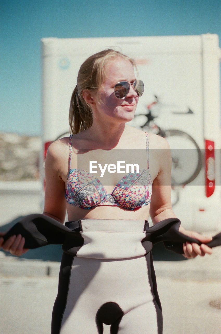 Young woman wearing sunglasses and bikini top against sky