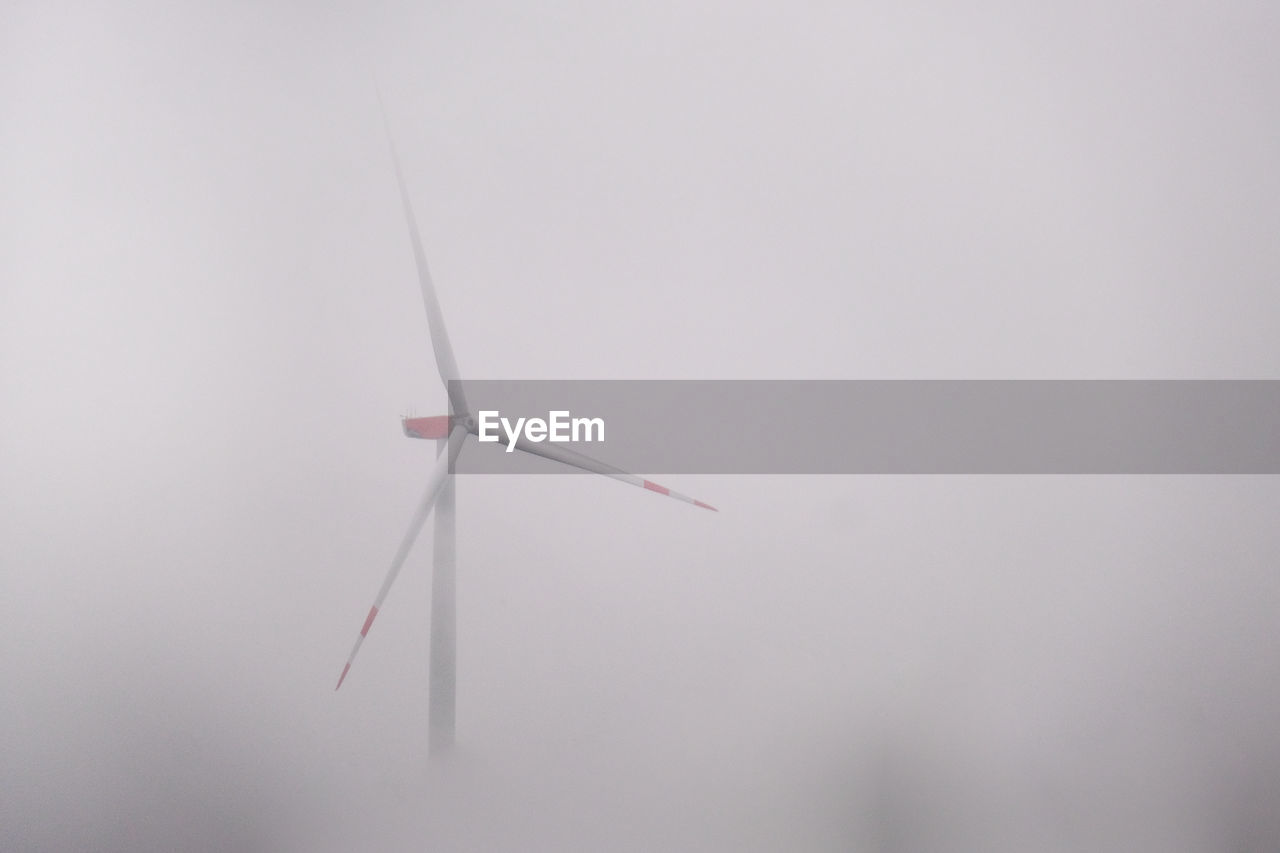 Low angle view of wind turbines against grey sky