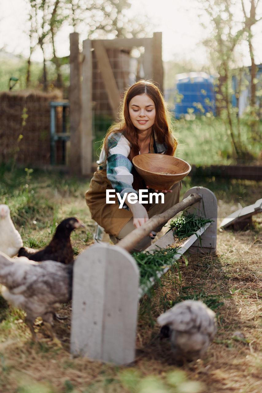 Smiling woman feeding chickens in farm