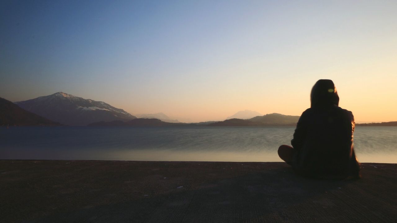 Person sitting on pier during sunset