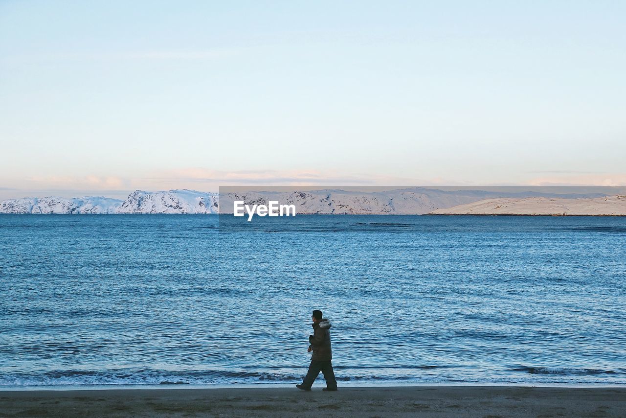 Side view of man walking at beach against sky