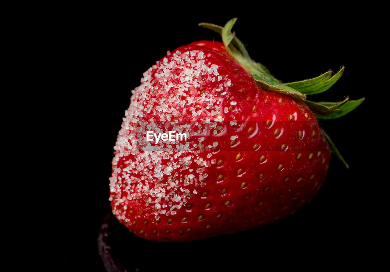 Close-up of strawberry covered with sugar against black background