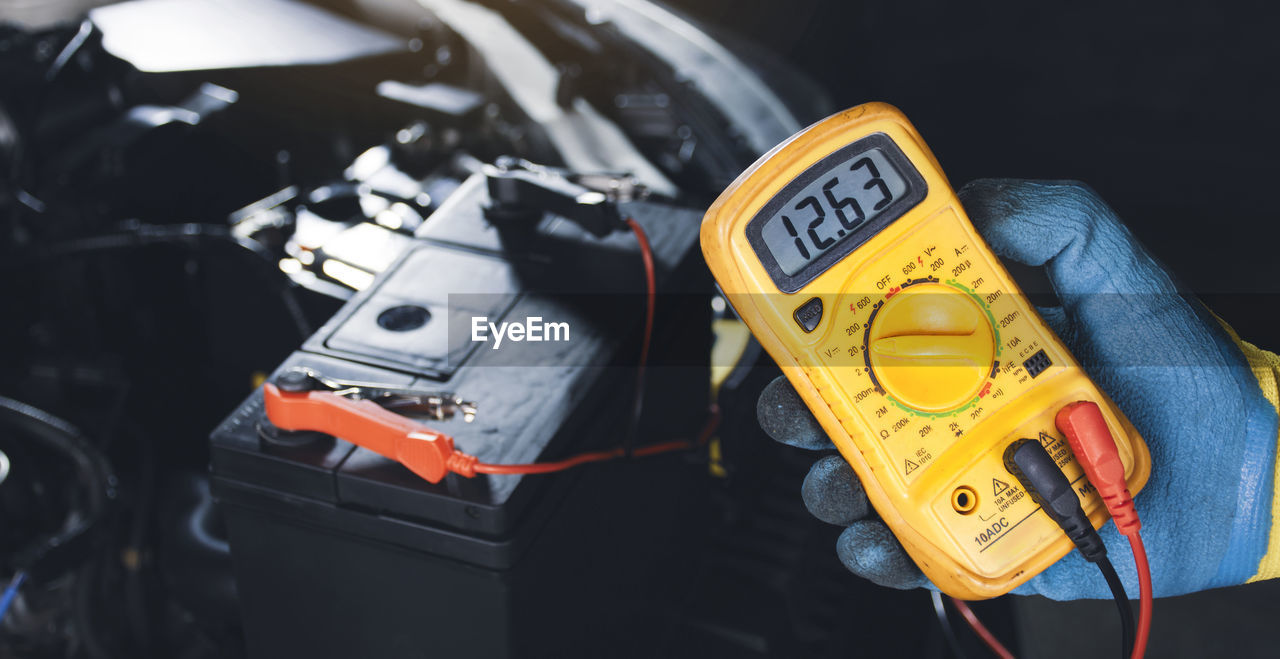 Mechanic checking car battery voltage stable with digital multimeter