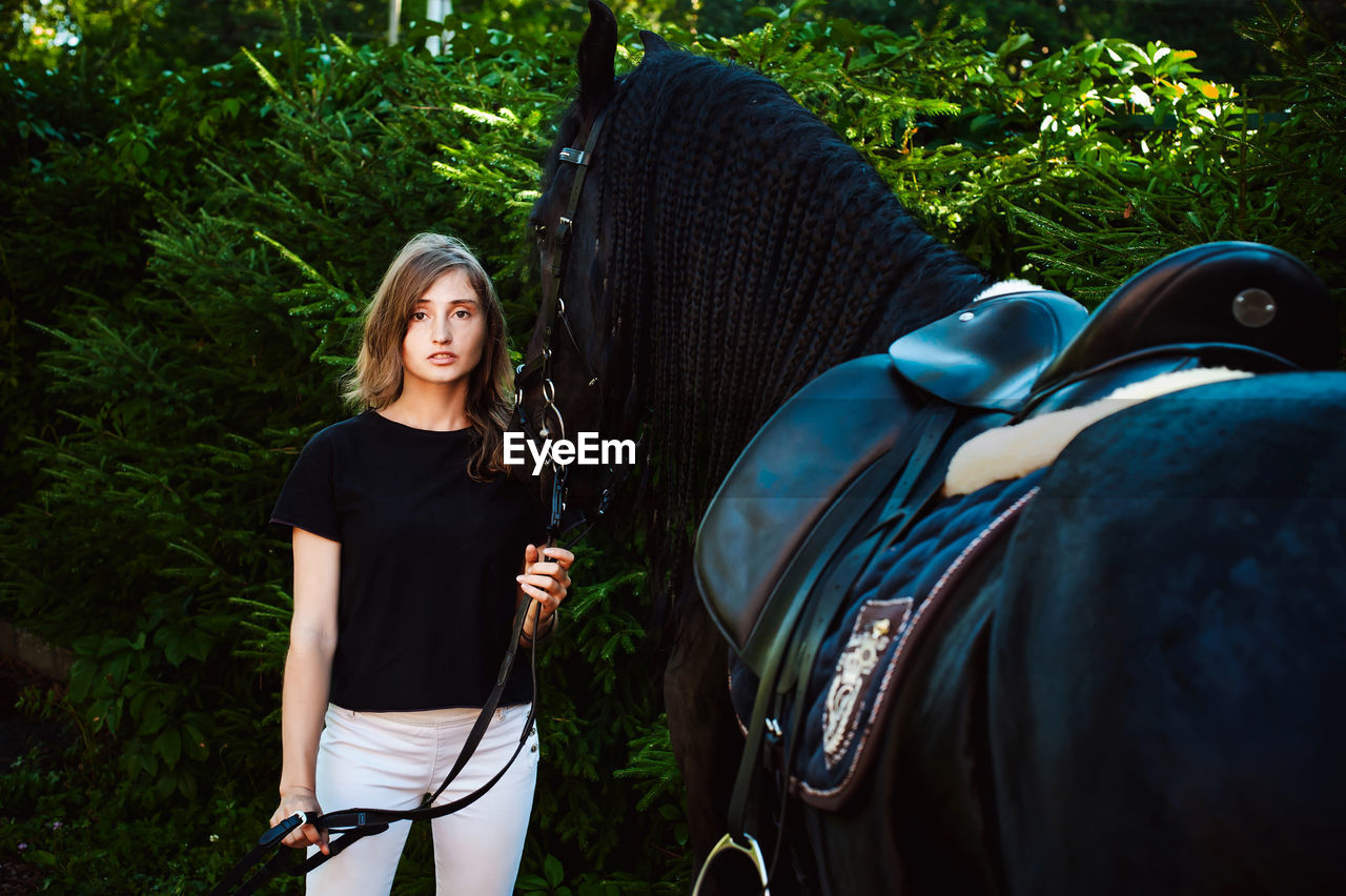 Portrait of young woman standing with horse against trees